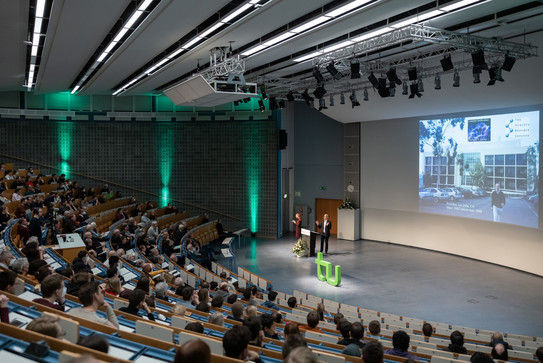 A man is giving a presentation in a lecture hall where several people are sitting. 