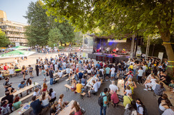 Vor einer Musikbühne sind viele Menschen stehend und auf Bierzeltbänken sitzend versammelt.