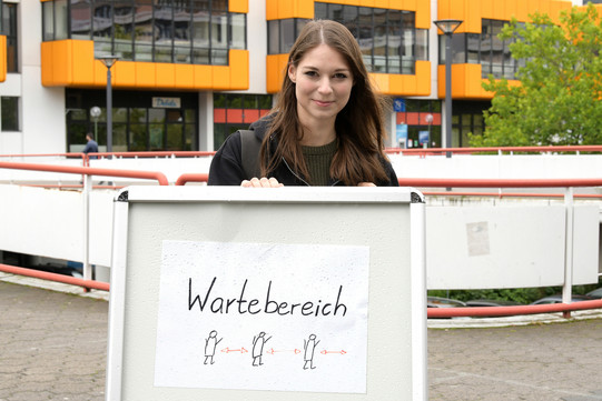 Eine Frau steht hinter einem Hinweisschild, das den Wartebereich der UB anzeigt.