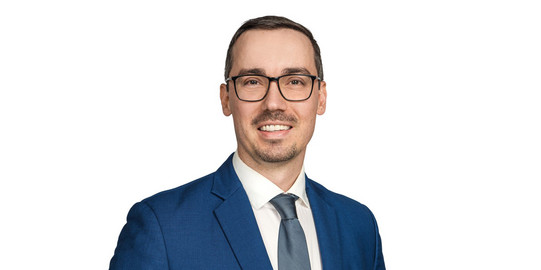 Derek Remes Portraitfoto eines Mannes im Anzug mit Brille vor einer weißen Wand