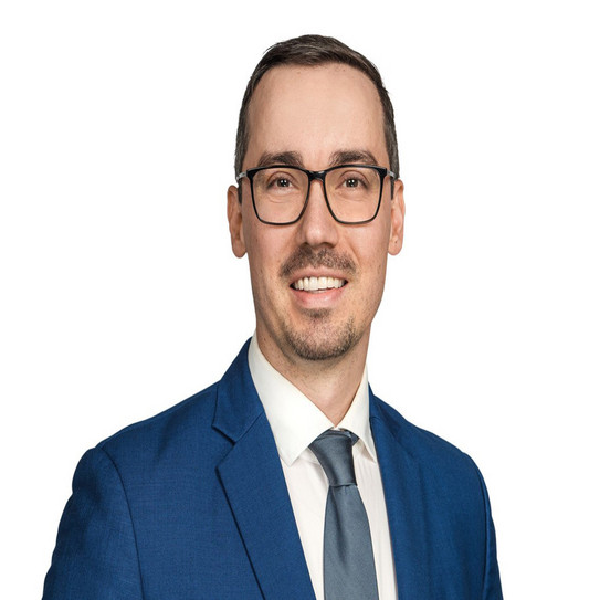 portrait picture of a man in a suite with glasses in front of a white wall