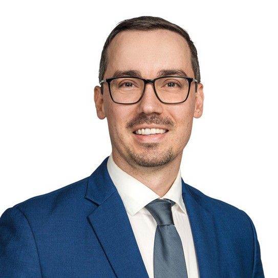 Portraitfoto eines Mannes im Anzug mit Brille vor einer weißen Wand
