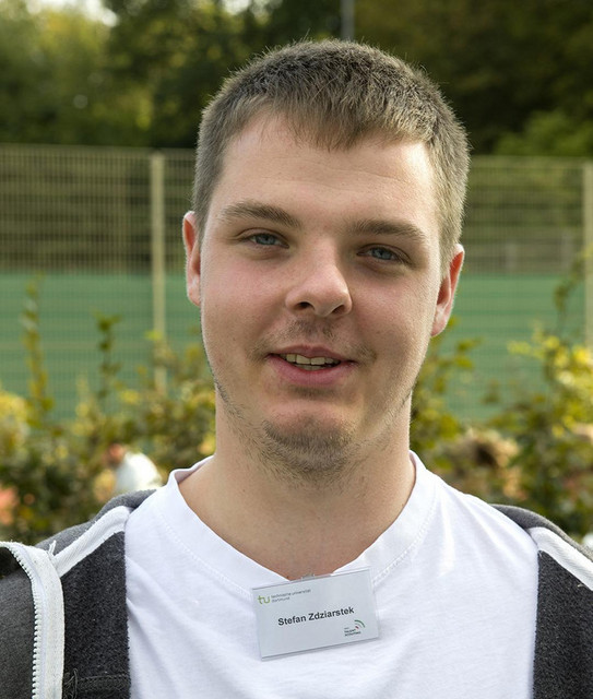 Foto von einem Jungen und er Trägt ein weißes Oberteil an dem ein Namensschild hängt