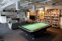 A room with kitchenette, table soccer, armchairs, bookshelf, dart board and pool table.