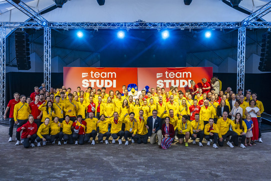 Gruppenfoto: Menschen in Trainingsanzügen vor einem Bühne.