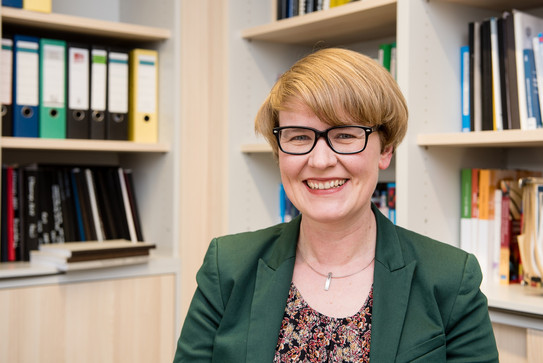Prof. Ricarda Steinmayr Porträt einer Frau mit Brille. Im Hintergrund Bücherregale.