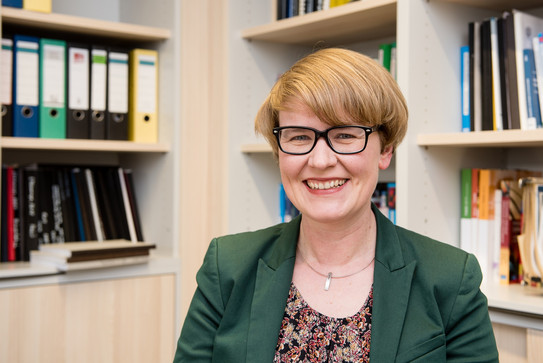 Porträt einer Frau mit Brille. Im Hintergrund Bücherregale.