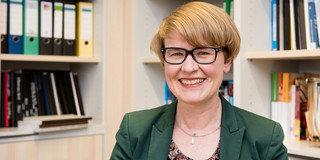 Portrait of a woman with glasses. In the background bookshelves.