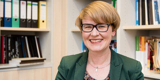 Prof. Ricarda Steinmayr Porträt einer Frau mit Brille. Im Hintergrund Bücherregale.
