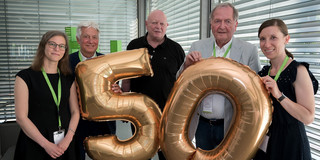 Five people stand side by side holding two balloons in front of them showing a five and a zero.