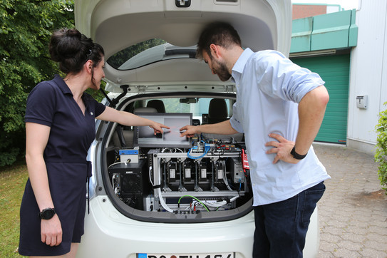 Automatisiertes Fahren Ein Mann und eine Frau blicken in den Kofferraum eines automatisiert fahrenden Autos.