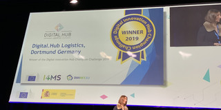 Eine große Leinwand auf einer Bühne, auf der das Digitial Hub Logistik Dortmund als Gewinner der Champions Challenge verkündet wird.