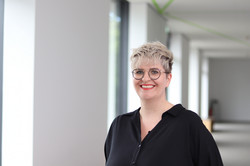 Portrait einer Frau mit Brille und kurzem blonden Haar in einem hellen Flur