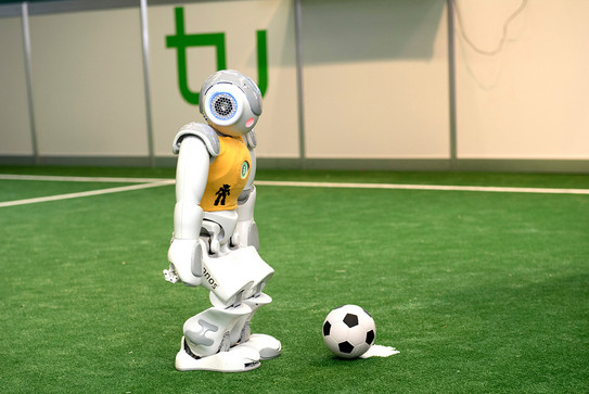 Fußballroboter Anstoß Ein Roboter mit gelbem Trikot steht mit einem Ball am Anstoßpunkt.