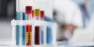 A few test tubes standing on a table, one test tube has the label "Covid".
