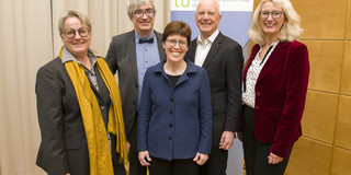 Gruppenfoto mit drei Frauen und zwei Männern. Im Hintergrund ist ein Aufsteller der TU Dortmund zu sehen.