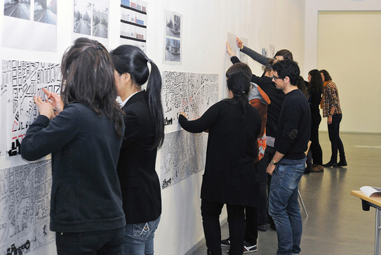 Architektur und Bauingenieurwesen Eine Gruppe von Studierenden schaut sich Baupläne an, die an einer Wand hängen.