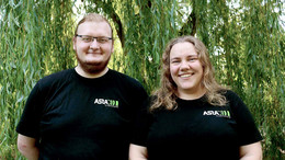 Juli Zwei Personen tragen schwarze Shirts mit AStA-Logo und stehen vor einer grünen Weide: Links Darius Weitekamp, rechts Lara Witte