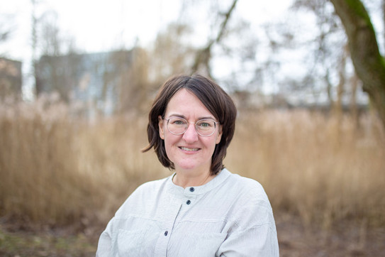 Porträtfoto von Prof. Katharina Kammeyer: Prof. Kammeyer hat schulterlange, dunkle Haare und verschränkt die Arme. Sie trägt eine helle Bluse und eine Brille.