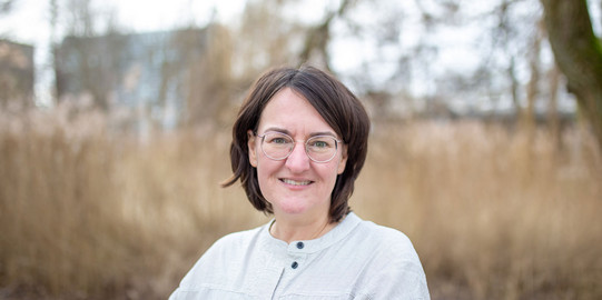 Porträtfoto von Prof. Katharina Kammeyer: Prof. Kammeyer hat schulterlange, dunkle Haare und verschränkt die Arme. Sie trägt eine helle Bluse und eine Brille.