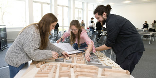 Drei Studierende arrangieren Häuser in einem Architekturmodell.