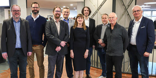Eröffnung DoBaS Acht Männer und eine Frau posieren gemeinsam für ein Gruppenfoto.