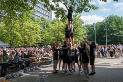 Das Cheerleading-Team der TU Dortmund zeigt eine Pyramidenfigur auf dem Martin-Schmeißer-Platz. Im Hintergrund ein großes Publikum an Picknick-Tischen und im Stehen.
