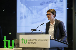 Eine Frau hält eine Rede an einer Kanzel mit TU-Logo