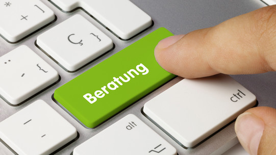 Finger drückt grüne Taste mit dem Wort 'Beratung' auf weißer Computertastatur