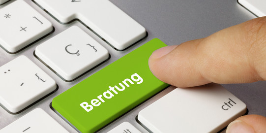 Finger pressing green key labeled 'Beratung' on white computer keyboard.