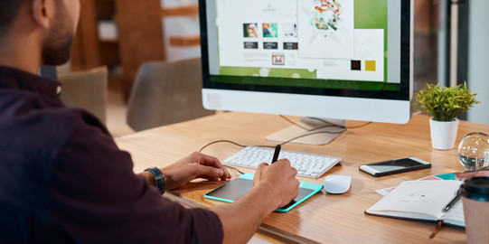 Foto: Eine Grafikdesigner sitzt am Computer und arbeitet an einem Design.