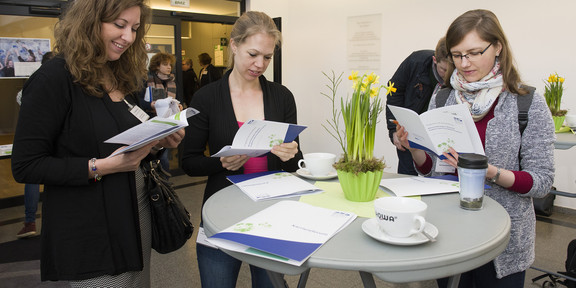 Three women stand around a high table and look at information material from the career forum.
