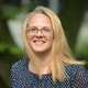 Das Porträtfoto zeigt Prof. Angela Madeo. Sie hat blonde, mittellange Haare und trägt ein blau-weißes Oberteil. Im Hintergrund sind verschwommen Büsche und Baumstämme erkennbar.