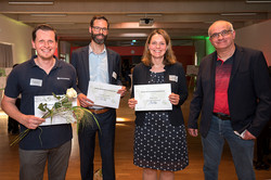 Gruppenfoto mit Rektor und drei Gewinner*innen, die Schecks und Blumen in den Händen halten