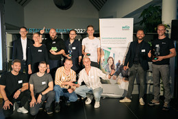 Die Die Jury des TU Start-up Awards Dr. Martin Oettmeier, Prof. Tessa Flatten und Nic Lecloux stehen mit den Start-up-Teams neben einem Banner von der wilo Foundation.