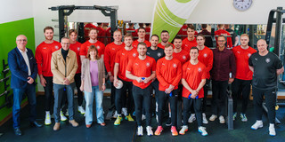 Group photo of the men's national handball team in the TU Dortmund University gym with the president, chancellor, director of human resources, and director of university sports