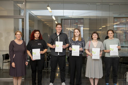 Rundgang Kunst Preisträger*innen Gruppenfoto von fünf Studierenden mit Urkunden vor einer Glaswand. Links steht Prof. Wiebke Möhring.