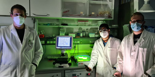 Ein Mann links und eine Frau und ein Mann rechts im Labor mit weißen Kitteln.