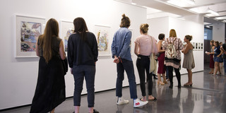 Besucher einer Ausstellung schauen sich Bilder an, die an einer Wand hängen.