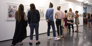 Besucher einer Ausstellung schauen sich Bilder an, die an einer Wand hängen.