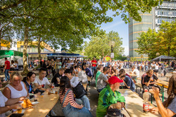 Viele Menschen sitzen an Tischen im Schatten eines Baumes