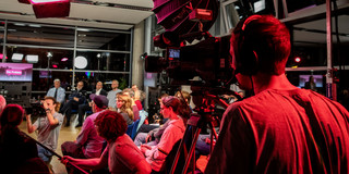 Foto: Ein Kameramann filmt eine sitzende Gruppe bei einer Studioveranstaltung.