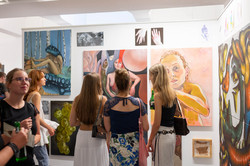 Im Zentrum des Bildes sind drei weiblich gelesene Personen von hinten zu sehen, die sich Kunstwerke anschauen. Links im Bild sind weitere Kunstinteressierte zu sehen.
