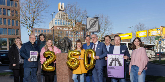 Foto: Eine Gruppe von Personen steht mit goldenen Ballons und Plakaten im Stadtzentrum von Dortmund.