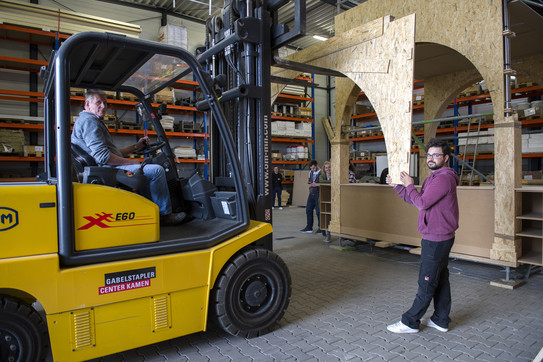 Projekt Paradiesgarten Ein Gabelstapler hebt ein Bauteil für den Paradiesgarten hoch. Ein Mann stützt das Bauteil.