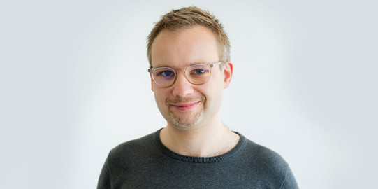 Porträtfoto von Prof. René Westerholt vor einem hellen Hintergrund: Prof. Westerholt trägt eine Brille und ein dunkles Oberteil.