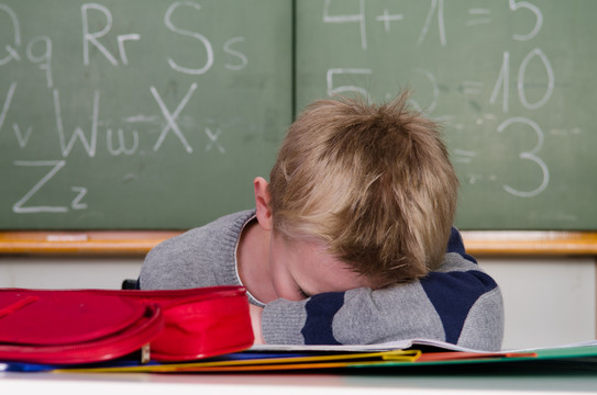 Ein Schulkind sitzt resigniert an seinem Pult im Klassenzimmer