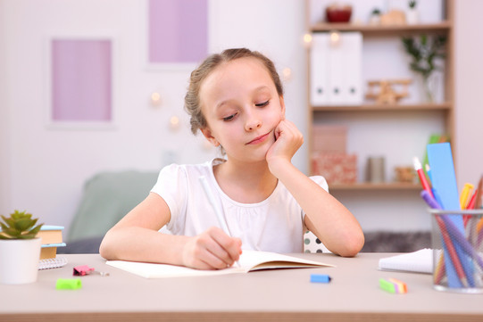 Eine junge Schülerin sitzt an einem Schreibtisch und schreibt in ein Heft. 