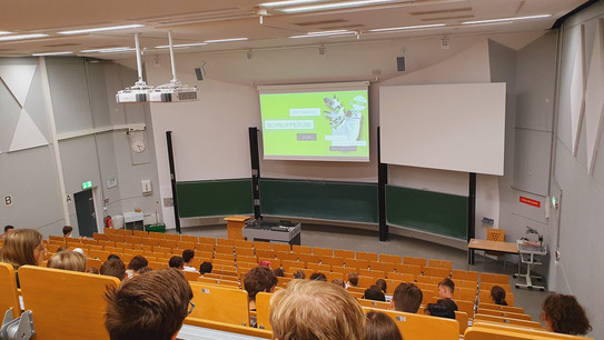 Teilnehemende sitzen im Hörsaal und schauen auf die Präsentation der SchnupperUni