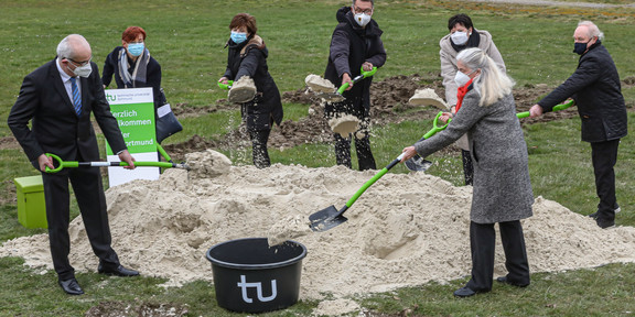 Erster Spatenstich für Forschungsbau CALEDO am Campus Nord Sieben Personen stehen auf einer grünen Wiese auf dem Campus Nord der TU Dortmund und setzen einen Spatenstich in den Sand.